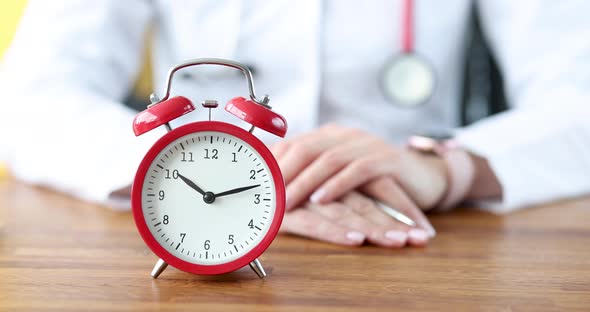 Red Alarm Clock Stands on Desktop Against Background of Doctor  Movie