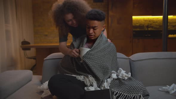 Caring Young Adult Wife Giving Hot Tea Drink To Sick African American Husband