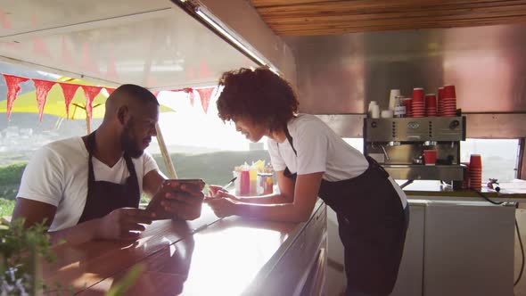 African american couple wearing aprons using digital tablet and taking notes in the food truck