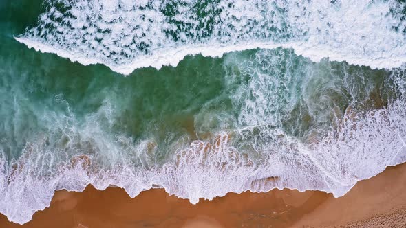 Top Aerial View of Foam Waves Break on Orange Colored Sand Beach