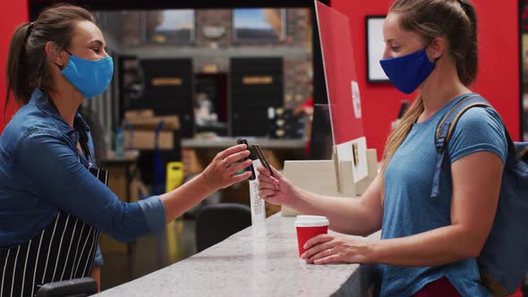 Woman wearing face mask making payment using contactless credit card at a cafe