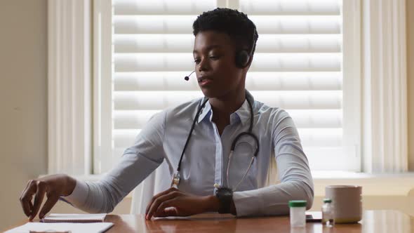 Portrait of african american female doctor wearing phone taking notes while having a video call