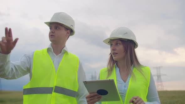Power Lines Man and Woman Engineers with a Tablet in Their Hands Check the Progress of the