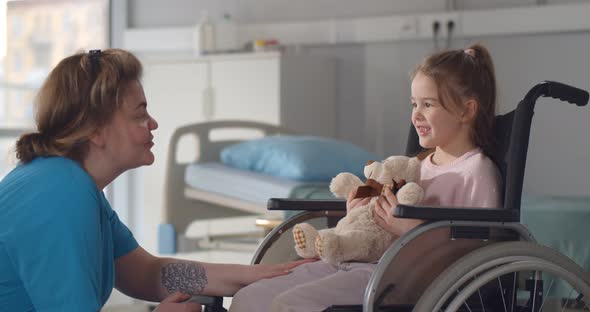 Child Patient in Wheelchair Sitting in Hospital Ward Talking to Female Nurse