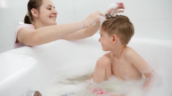 Happy Smiling Mother Playing with Her Son Washing in Bath with Soap Foam