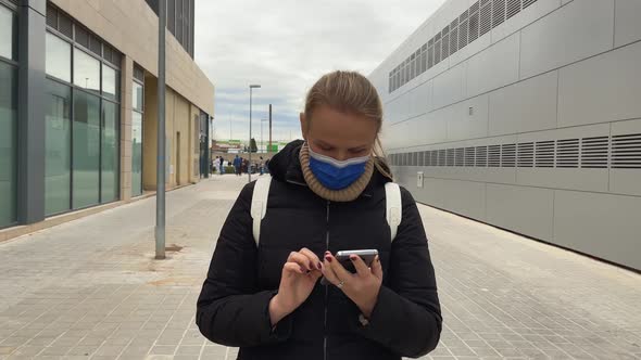 Woman in mask walking to work and chatting online on smartphone