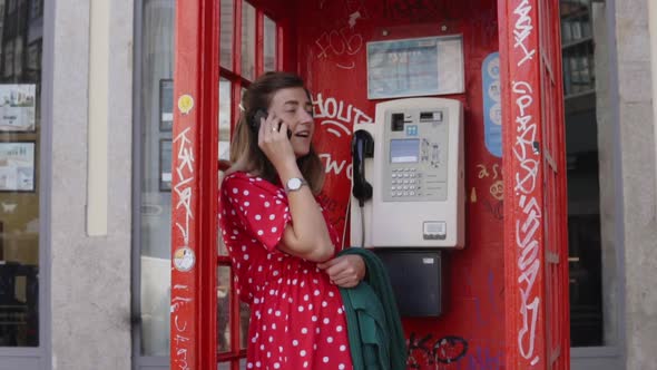 Young Woman Is Talking on Mobile Phone in Telephone Box