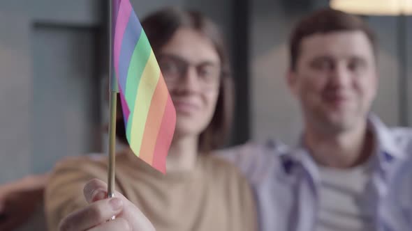 Close-up of Rainbow Lgbt Flag in Male Hand with Two Blurred Men Smiling at the Background. Positive