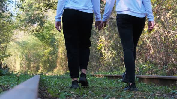 Twins Girls Holding Hands Walking Along Railroad Tracks