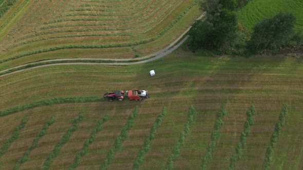 Silage Bale Wrapper And Grass Turner Farm Machinery At Work On Farmland, Norway. aerial