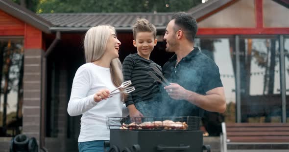 Happy Family Cook Meat on Grill. Father and Mother with Son Fry Sausages on Grill and Smiling