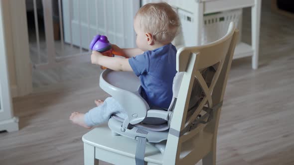 Cute Kid with Baby Straw Feeding Cup Sitting in Booster Seat One Year Old Toddler Watching Tv