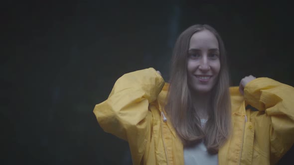 Portrait of Caucasian Girl Traveler in a Yellow Raincoat Near a Waterfall in the Forest