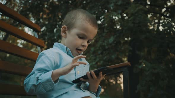 Little Boy Playing Video Games on His Smartphone Outdoors.