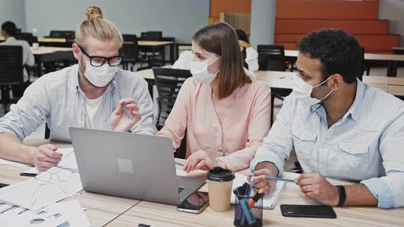 Diverse Colleagues in Protective Masks Working at Laptop Discussing New Business Project Sitting at