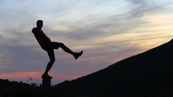 Dark silhouette of a hiker balancing on a stone in evening mountains.