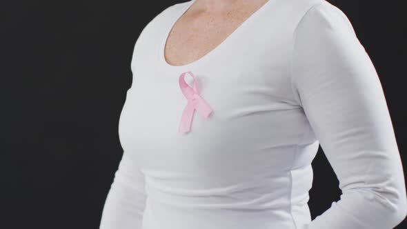 Mid section of a woman showing the pink ribbon on her chest against black background