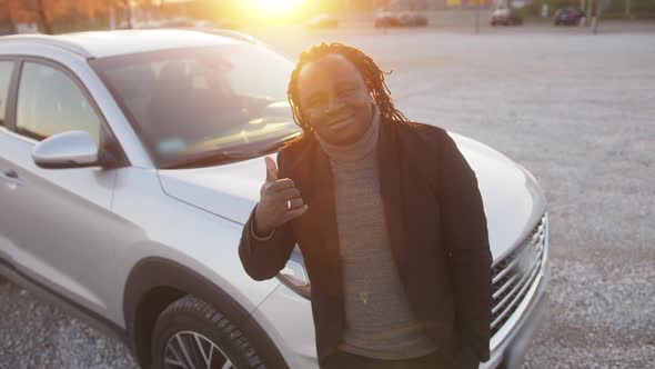 Young African American Man Showing Thumb Up in Front of His New Vehicle on the Road on Sunset