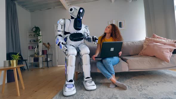 Young Woman Is Operating a Laptop and Talking To the Robot. Robot, Human-like Cyborg Concept.