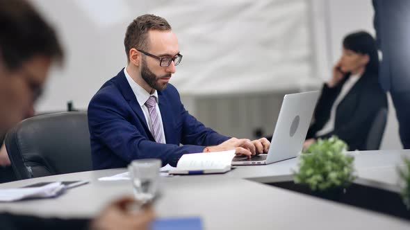 Trendy Businessman Focused Typing on Laptop Working with Business People at Office Routine