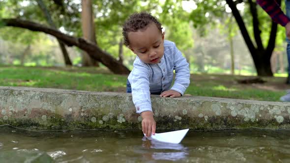 Little Mixed-race Boy Playing with Paper Ship in Park
