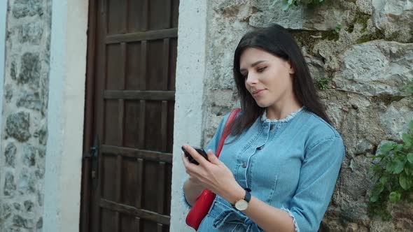 Pretty young woman with brunette hair in denim overalls  texting on her phone