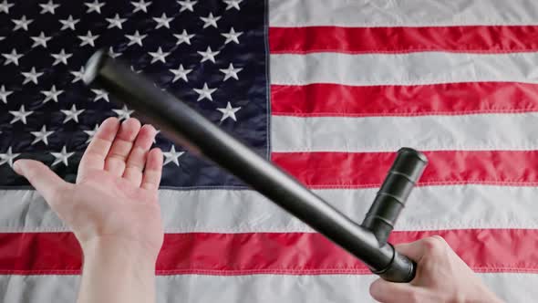 Caucasian Hands Holding Black Rubber Police Tonfa Baton Over Blurry US Flag