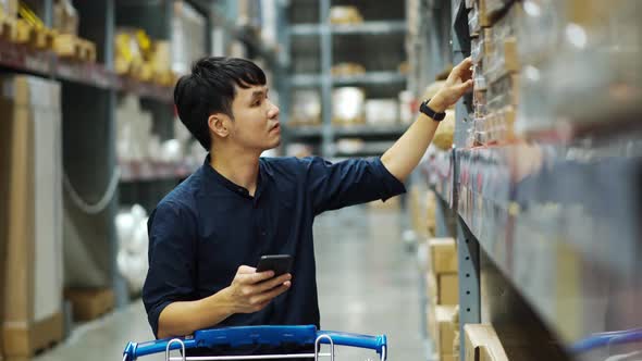 man looking at his mobile phone and shopping in the warehouse store