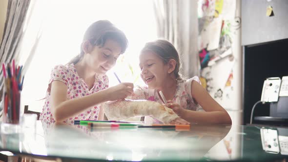 Concept of Care in the Family the Child Paints the Plastered Hand of Her Sister in Bandage