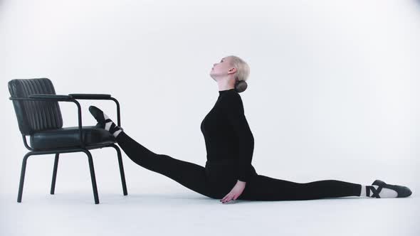Young Blonde Woman Ballerina Putting on Her Leg on the Chair and Bending Her Back