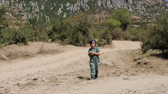 Boy Child in a Green Jumpsuit Carries a Stone While in the Mountains