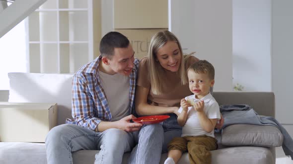 Happy Family Couple with Kid Son Eating Snacks on Moving Day in New Home