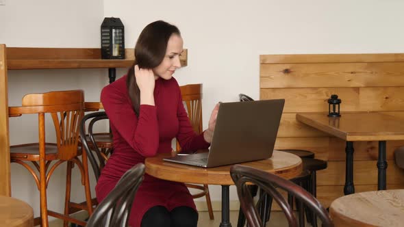 Business Woman in Red Dress Working at Laptop Computer in Cafe Drinking Latte Coffee