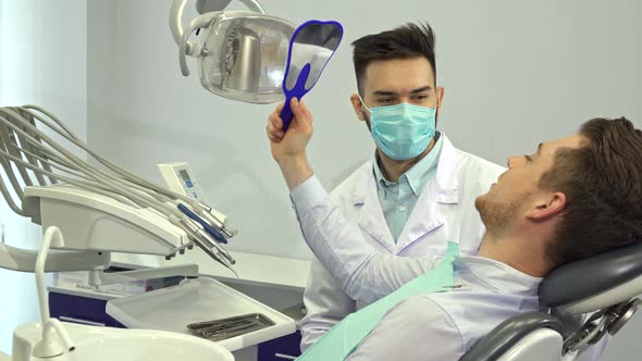 Patient Looks at His Teeth in the Mirror at the Dentist's Office