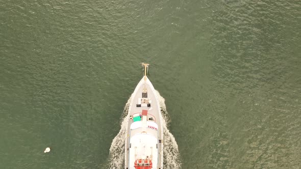 A top down aerial shot directly above a fishing boat, heading out to sea on a cloudy morning. The dr