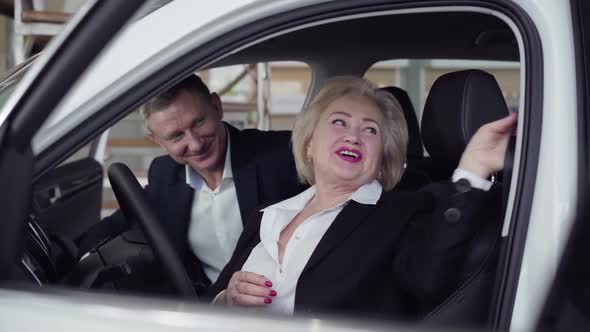 Confident Senior Caucasian Woman Fastening Seat Belt in New Automobile in Showroom. Positive Wealthy