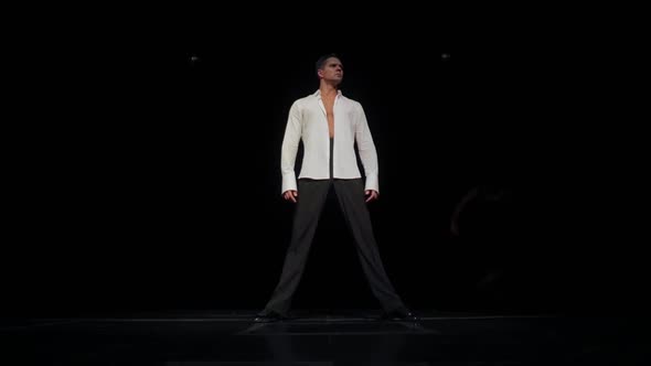 Serious Young Man on Black Stage in Unbuttoned White Shirtlegs Wide Apart Dancer's Poseturning Head