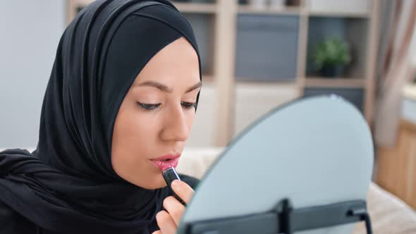 Closeup Arabic Female in Black Hijab Applying Lipstick on Lips in Front of Mirror at Living Room