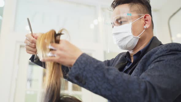 Asian professional male hairstylist combing and using scissors cutting woman's hair in beauty salon.