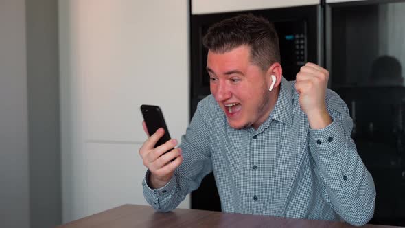 Excited young adult man looking at smart phone and shocked about good news seen on gadget screen