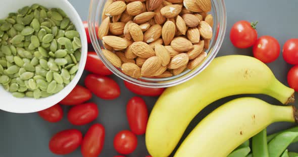 Video of fresh fruit and vegetables and bowls of nuts and seeds over grey background