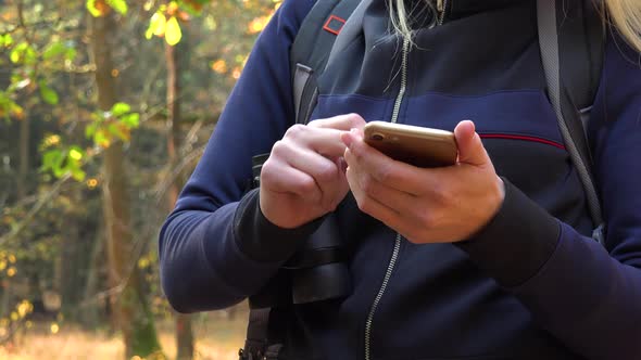 A Hiking Woman Works on a Smartphone in a Forest - Closeup