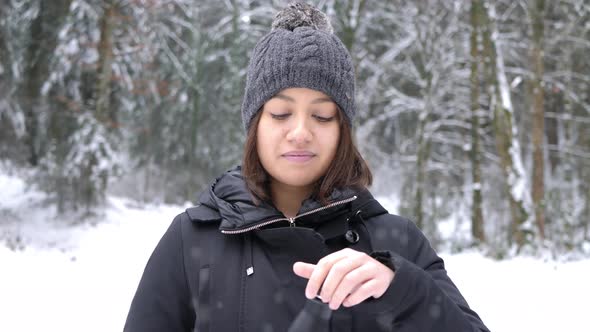 Young caucasian woman drinking hot tea from thermo bottle in the park on snowy day