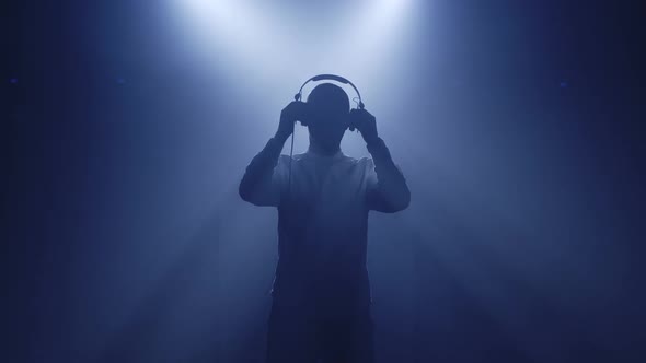 Backlit Silhouette of Dj Man Standing in Dark Nightclub Disco Putting Headphones on To Listen Music