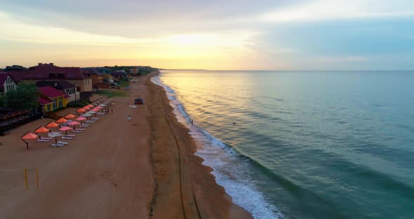 Flying along a sandy beach over the edge of the calm sea in the evening against the orange 4K 30fps