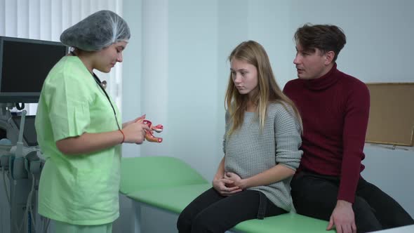Young Female Obstetrician Showing Vagina Anatomy Model Talking with Pregnant Woman and Smiling Man