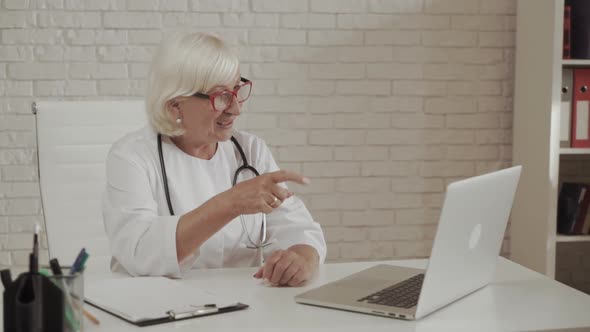 Senior Confident Female Doctor in Eyeglasses Sits in the Cab and Using Laptop for Online