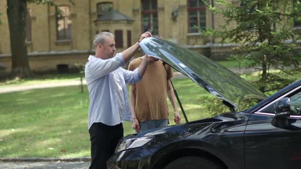 Confident Middle Aged Man Helping Stressed Guy with Broken Car on Summer Road