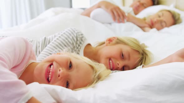 Smiling kids relaxing on bed while parents sleeping in background 4k