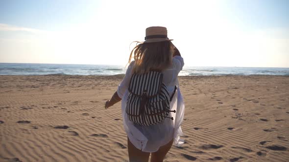 Happy Girl in Bikini and Shirt with Backpack Running on the Beach To the Sea. Beautiful Woman